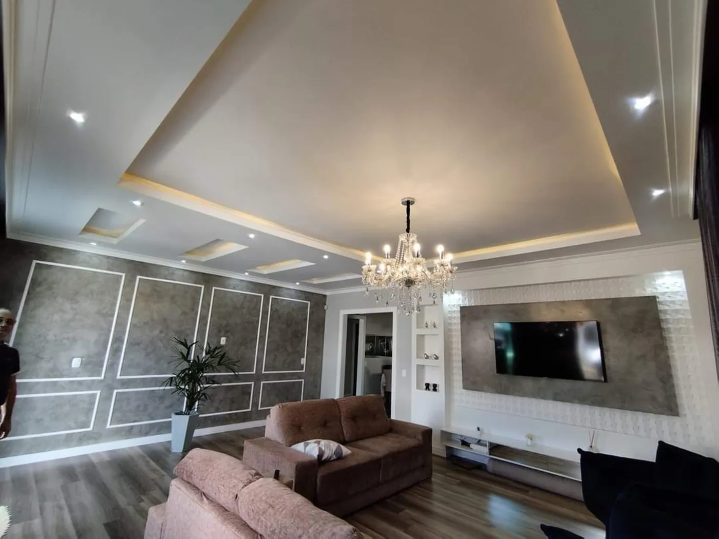 Sala com forro rebaixado em gesso, sanca com iluminação embutida e painéis em relevo na parede